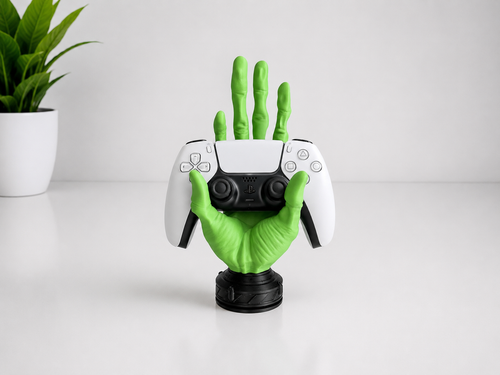 A green glove-shaped game controller stand holding a white and black Xbox Series S controller, set on a white surface with a small potted plant in the background.