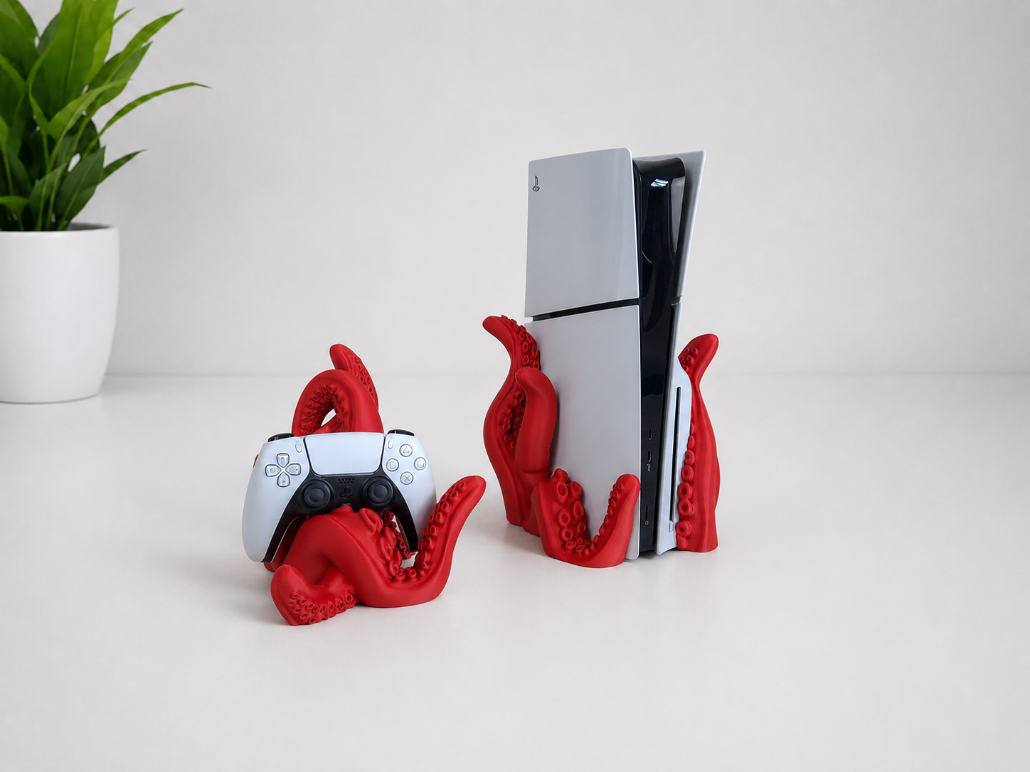 Red octopus-themed game console stands holding a white and black PlayStation 5 console and a matching controller, shown on a white tabletop with a small green plant in the background.