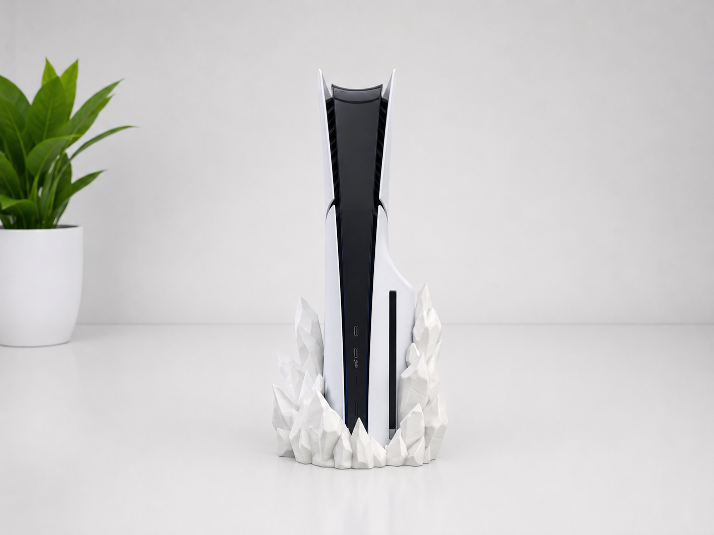 A white and black PlayStation 5 console standing upright on a sculptural white crystal-like base, set against a clean white background with a small green potted plant on the left.
