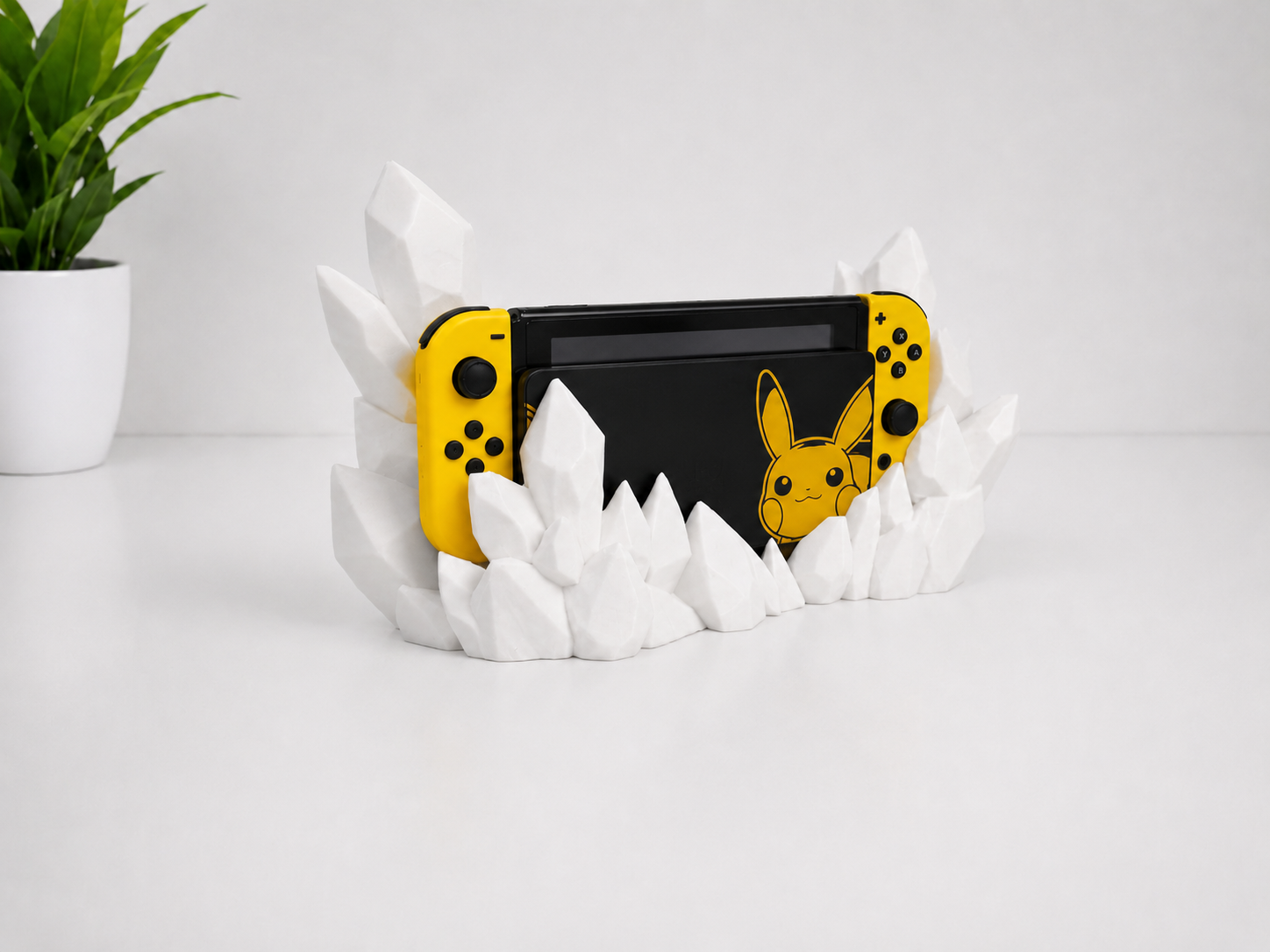 A black Nintendo Switch console with yellow Joy-Con controllers and a Pikachu graphic skin, displayed in a white crystal-shaped stand on a white surface against a white background.